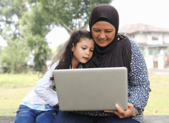 A girl and a woman sit together, looking at a laptop screen